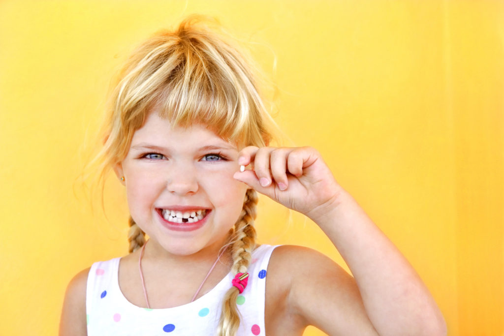 girl smiling with fallen tooth in her hand