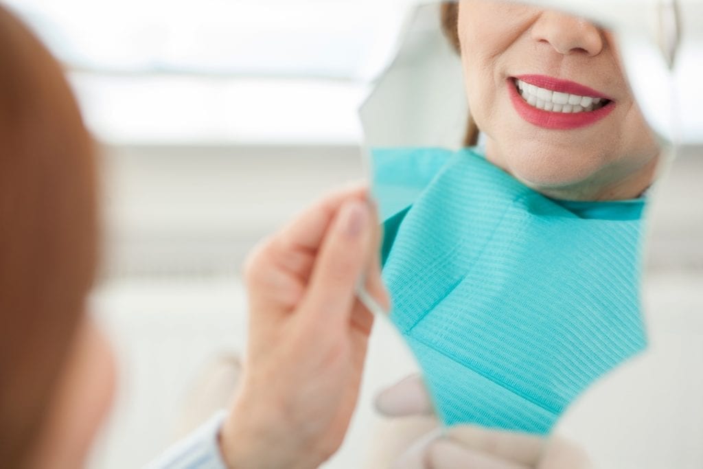 older woman looking at her new smile after dental treatment