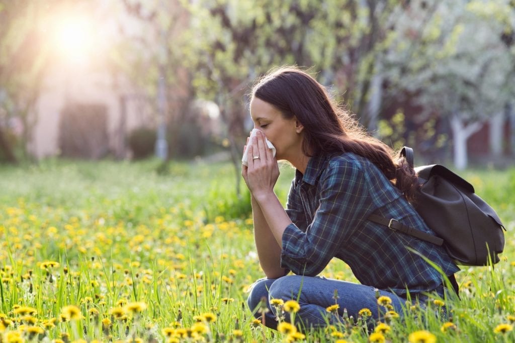 woman sitting in a field of flowers blowing her nose
