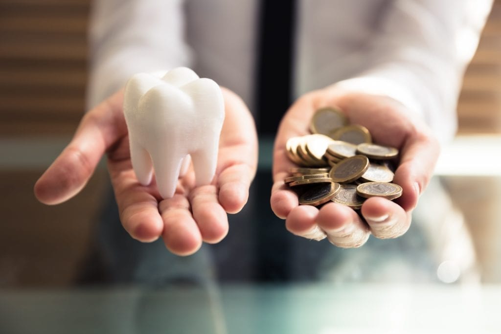 one hand holding giant tooth and one hand holding coins