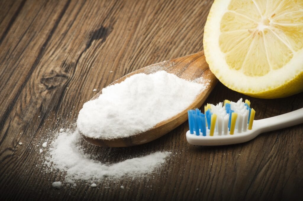 scoop of baking soda and half a lemon by a toothbrush